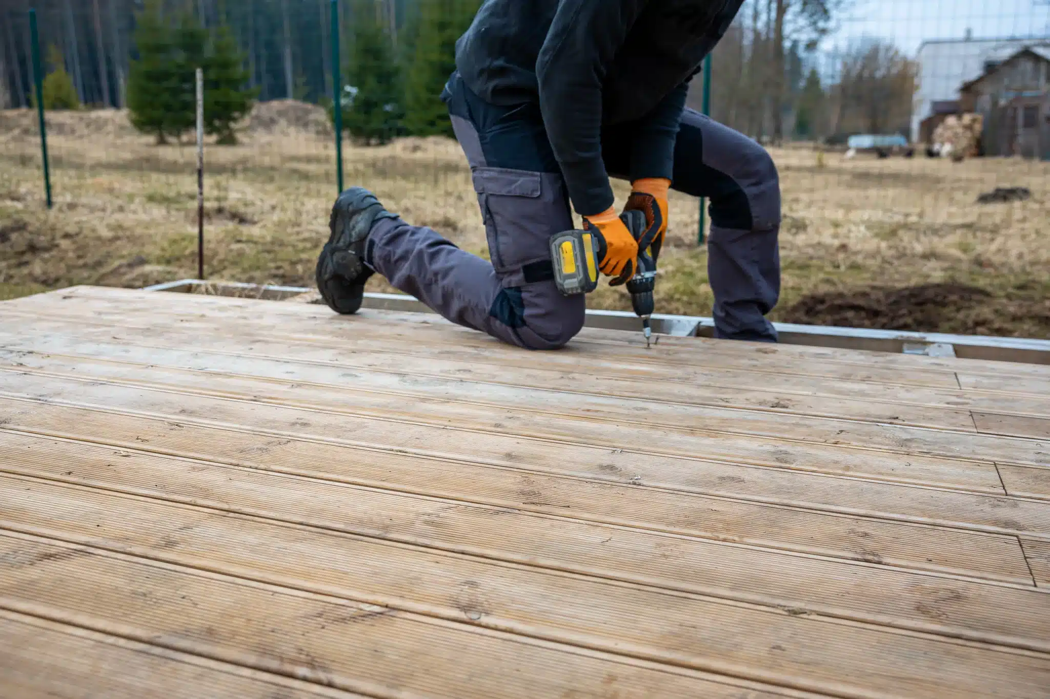 Ouvrier montant une terrasse en bois sur un terrain.