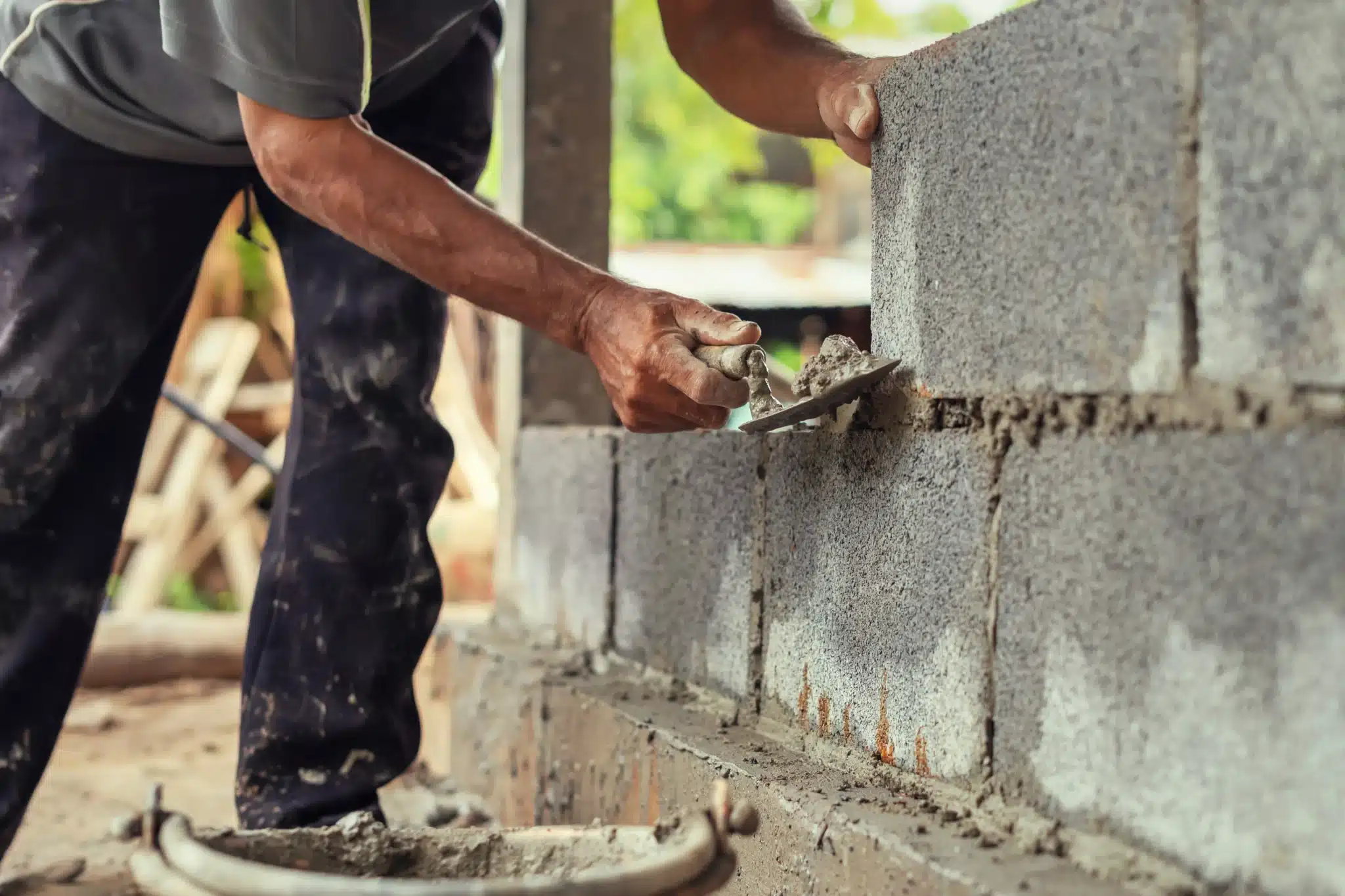 Ouvrier utilisant une truelle pour assembler des blocs de béton dans la construction d'un muret extérieur.