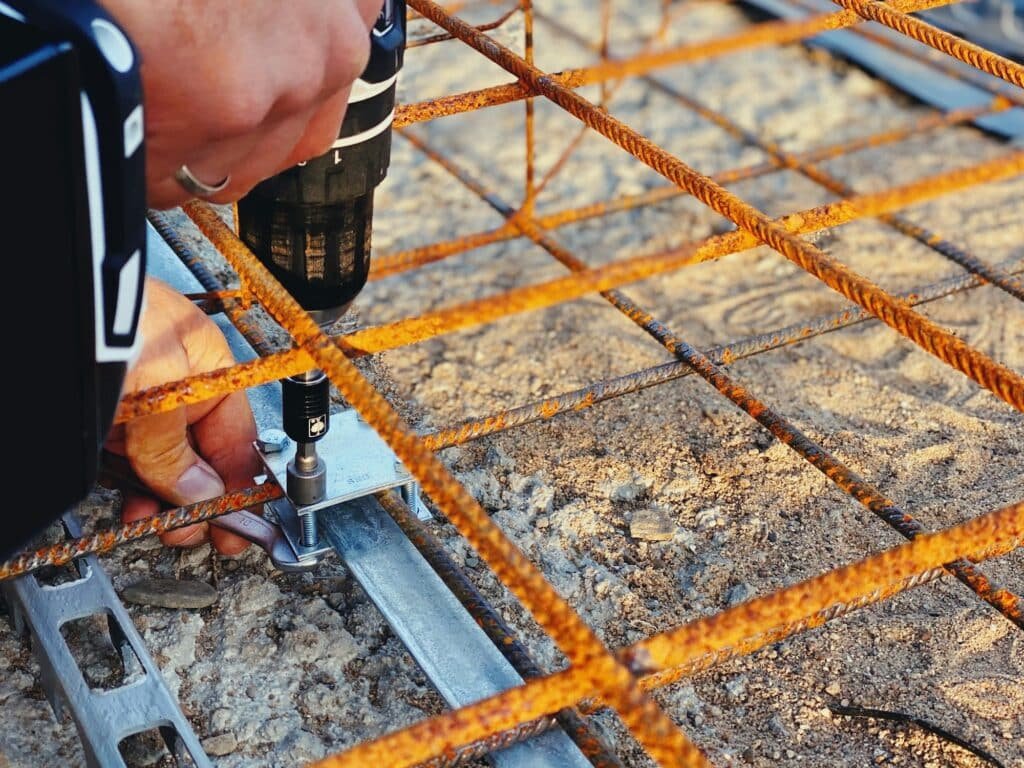 Ouvrier utilisant une perceuse pour installer des barres de renforcement sur un chantier de construction.