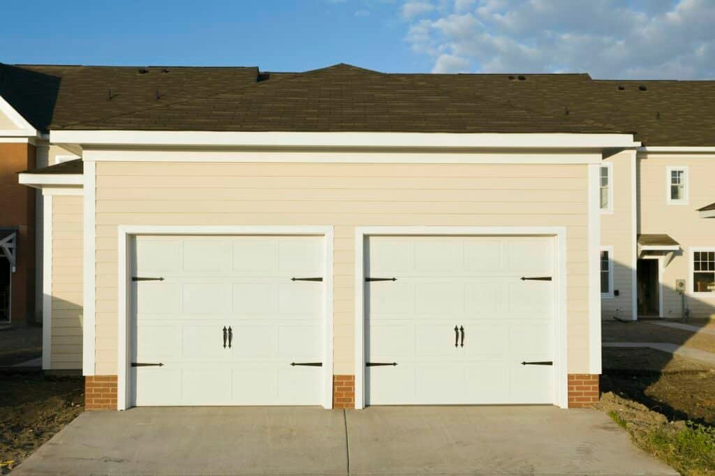 Façade extérieure d'un garage double avec des portes blanches et des poignées noires.