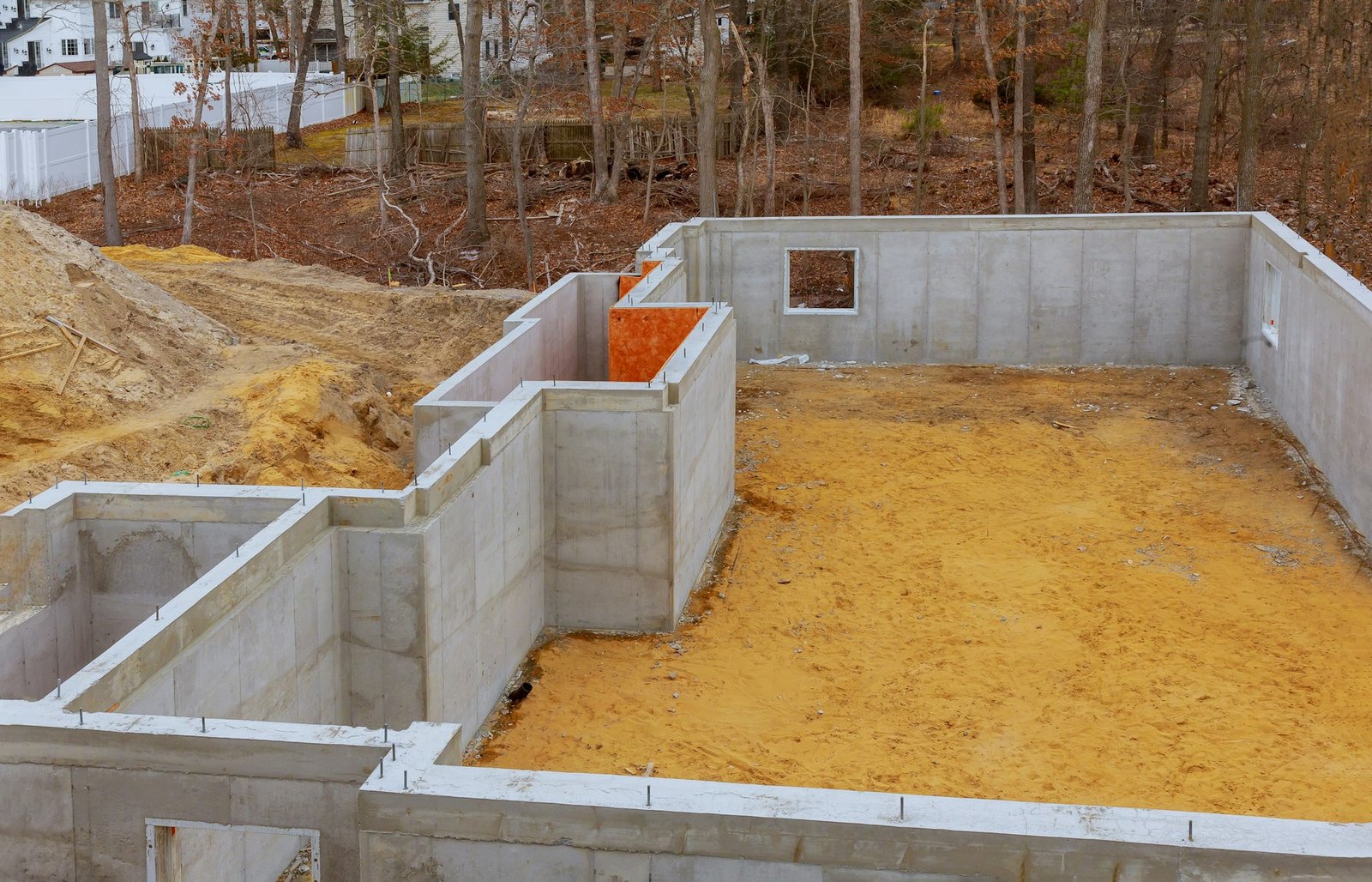 Fondations en béton d'une future maison en construction avec forêt à l'arrière-plan.