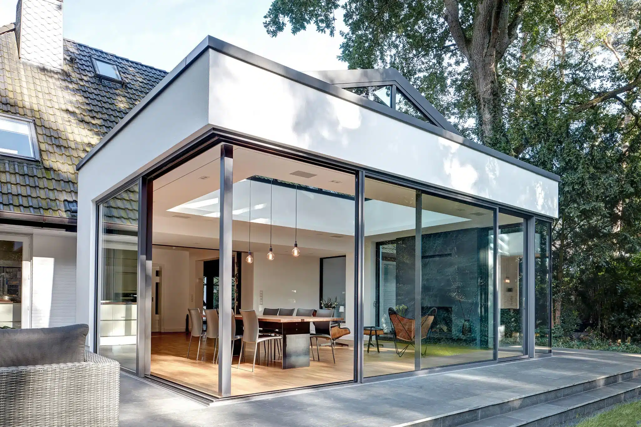 Extension contemporaine avec grandes fenêtres du sol au plafond donnant sur un jardin arboré.